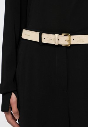 Cinturón de cuero beige con hebilla dorada, detalles cosidos y un sutil estampado de logo, usado sobre una prenda negra.