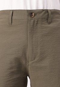 Pantalons vert olive en tissu texturé, dotés d'une fermeture à bouton, de passants de ceinture et de poches latérales avec des détails de couture visibles.