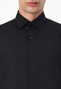 Black button-up shirt with a spread collar, featuring a smooth texture and six black buttons down the front, designed for a fitted look.
