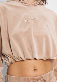 Corto hoodie in velluto beige con orlo arricciato, caratterizzato da un logo ricamato sul petto e un cappuccio con dettaglio a lacci.