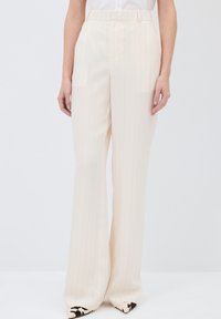 Pantalons larges crème avec des rayures verticales, présentant une taille haute et une texture lisse. Détails avec des chaussures à bout pointu.