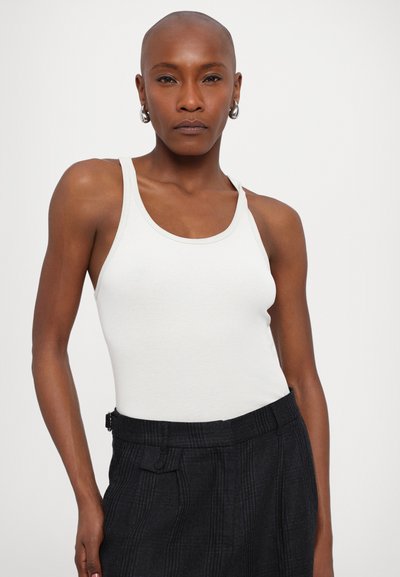 Hvid ribbet tanktop med brede stropper, parret med sorte ternede bukser. Blødt stof, tætsiddende design og subtil kontrastkant ved udskæringen.