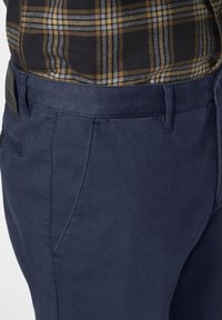 Navyblaue Hose aus strukturierter Stoffqualität, mit vorderen Taschen, einer taillierten Passform und einem schwarzen Logo-Patch am hinteren Bund.