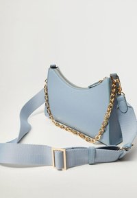 Borsa a spalla in pelle azzurro chiaro con forma curva, dotata di una catena dorata e di una tracolla in tessuto regolabile. Chiusura con zip nella parte superiore.