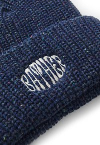 Navy blue knitted beanie with a textured pattern and a white embroidered logo patch on the front. Soft, warm material.