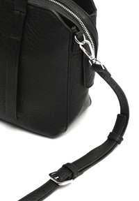 Sac à main en cuir noir avec surface texturée, fermeture éclair en argent et bandoulière réglable avec matériel en métal. Forme rectangulaire compacte.
