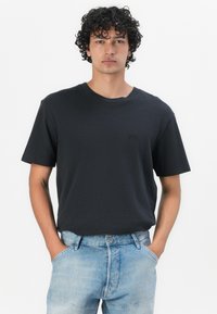 Zwarte T-shirt met korte mouwen en een ronde halslijn, subtiel logo detail, gedragen met lichtblauwe denim jeans met een relaxte pasvorm.