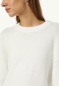 White knitted sweater with a ribbed round neckline and textured fabric. Features dropped shoulders and a relaxed fit.