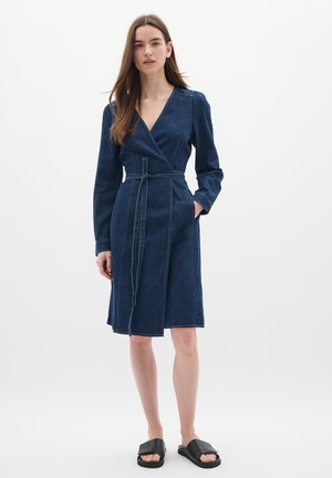 Denim wrap dress in dark blue with long sleeves, side pockets, and a fabric belt. Features contrasting stitching and a knee-length cut.