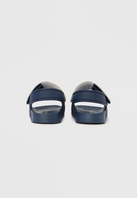 Sandalias deslizantes azul marino con un exterior de plástico liso, parte trasera abierta y suela texturizada que muestra un diseño delineado.