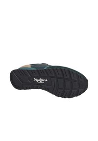 Suela de zapatilla de goma negra, con un patrón texturizado para mayor agarre, y con acentos en verde y beige en la parte superior para un contraste de color.