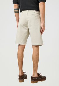 Lys beige shorts med lige snit og opslået kant. Har baglommer og et subtilt syet mønster. Bærers med brune snørebåndssko.
