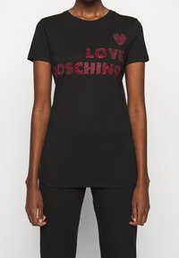Svart bomullströja med djärv röd strass-text "LOVE MOSCHINO" och hjärtdesign. Rund hals och korta ärmar, slät textur.