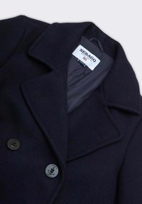 Cappotto peacoat in lana blu navy con design doppiopetto, ampio colletto a revers e due grandi bottoni rotondi neri con logo ancora. Fodera interna liscia.