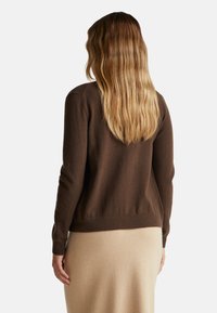 Brązowy sweter dzianinowy z okrągłym dekoltem i długimi rękawami, z prążkowanym dołem i gładką fakturą, w połączeniu z beżową spódnicą.