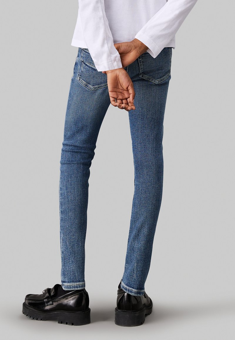 Blaue Baumwoll-Skinny-Jeans mit einer dezenten Textur, zwei Gesäßtaschen und einer schmalen Passform. Getragen mit schwarzen Plateauschuhen.