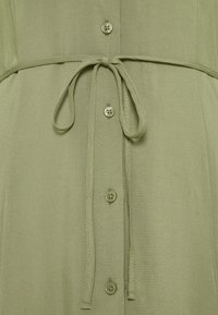 Olivenfarbiges Kleid aus weichem Stoff, das eine gebundene Taille, einen Knopfverschluss und eine subtile Textur aufweist. Die Knöpfe sind farblich passend und rund.