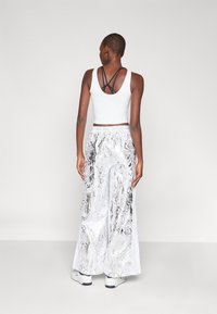 Biela crop top s čiernym vykrojením na zadnej strane, skombinovaná s lesklými širokými nohavicami so vzorom hadieho kože v striebornej a bielej farbe.