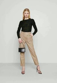 Top de manga longa texturizado preto, calças bege ajustadas, mala preta com corrente, saltos pretos com tiras, contra um fundo cinza claro.