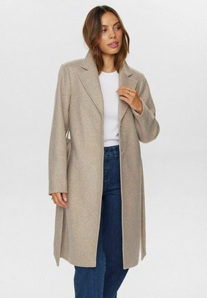 Beige wollen jas met een geknipt revers, lange mouwen en twee knopen. De stof lijkt zacht met een iets gestructureerd oppervlak.