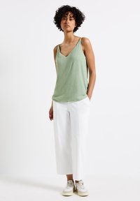 Lichtgroen getextureerd tanktop met een V-hals en dunne bandjes, gecombineerd met losse witte cropped broeken en beige sneakers.