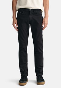 Mustat farkut slim fit -lelulla, joissa on klassinen viisi-tasku -muotoilu ja metalliosat. Yhdistetty mustiin tennareihin.