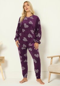 Violetti samettinen yöpuku, jossa on valkoisia sydänkuvioita. Paidassa on pitkät hihat ja pyöreä kaula-aukko; housuissa on istuvat hihansuut.