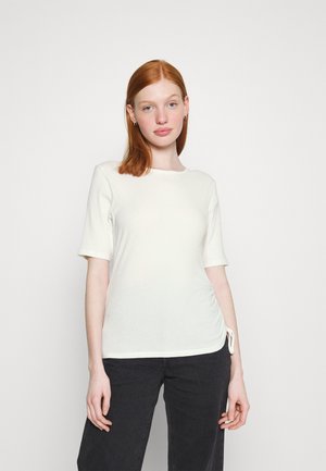 Valge ribaga T-särk lühikeste varrukatega ja ümmarguse kaelusega, külgedel kogumise detailiga, mis annab nedale liibuvama lõike. Kandmist mustade pükstega.