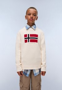 Pletený krémový svetr s norským vlajkovým designem v červené, černé a bílé barvě, nošený přes modrou kostkovanou košili. Outfit doplňují béžové cargo kalhoty.