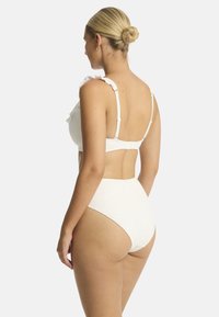 Weißes Bikini-Set aus strukturiertem Stoff, mit Rüschenrand am Oberteil, verstellbaren Trägern und hochgeschnittenen Unterteilen mit dezenter Detailgestaltung.