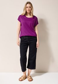 Lila kortärmad t-shirt kombinerad med mörk denim cropped byxor och ljusbruna sandaler, med en mjuk textur och avslappnad passform.