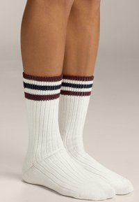 Calze bianche al ginocchio con texture a coste e dettagli a strisce borgogna, blu navy e bianco sulla parte superiore. Materiale liscio ed elastico.