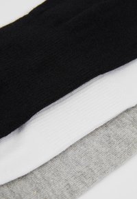 Drei Paar Socken gestapelt: schwarz, weiß und hellgrau. Jede hat eine glatte Textur mit gerippten Akzenten an den oberen Kanten.