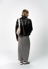 Giacca di pelle nera, vestito maxi grigio, borsa a tracolla beige con coulisse, sneakers bianche e nere. Texture liscia, vestibilità rilassata e stile casual.