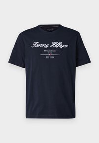 T-shirt bleu marine à manches courtes avec texte blanc "Tommy Hilfiger Established 1985 New York" imprimé sur le devant.