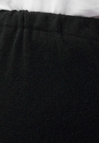 Svart stickad tyg med en texturerad yta och ett elastiskt midjeband, delvis dolt av ett vitt plagg ovanför.