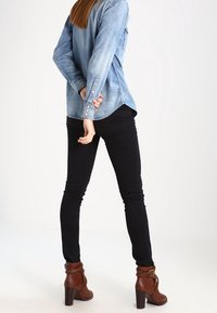 Ljusblå denimskjorta med långa ärmar, knapprad och en något rundad fåll, matchad med svarta skinny jeans och bruna ankelstövlar.