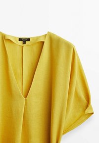 Haut en lin jaune avec un décolleté en V profond, des manches courtes et une coupe décontractée. Tissu texturé avec une apparence douce et respirante.