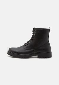 Botas de tobillo de cuero negro con puntera redonda, ojales trenzados y un acabado texturizado. Cuentan con una suela de goma resistente y una lengüeta en la parte trasera.
