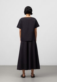 Czarny dwuczęściowy strój składający się z topu z krótkim rękawem o luźnym kroju oraz długiej spódnicy. Teksturowana tkanina z subtelnym wzorem. Minimalistyczny design.