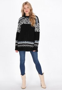 Schwarzer Strickpullover mit weißem und hellblauem gemustertem Einsatz, gerippten Bündchen und Saum. Kombiniert mit blauen Skinny Jeans und beigen Stiefeln.