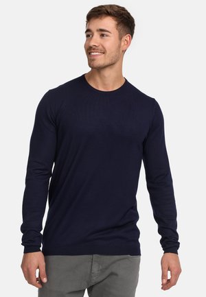 Navy long-sleeve sweater with a round neck, ribbed texture, and fitted silhouette. Paired with light gray trousers for contrast.