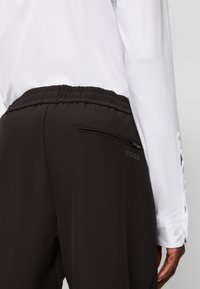 Svarta träningbyxor med elastisk midja och ficka med dragkedja, kombinerat med en vit långärmad skjorta med knäppärmar.