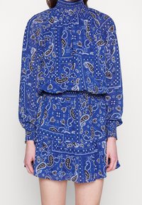 Vestido azul con estampado de paisley, de mangas largas, escote alto y cintura elástica. Hecho de un tejido ligero con un dobladillo con volantes.