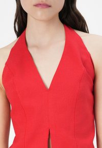 Haut à bretelles rouge avec un décolleté en V profond, fabriqué en tissu texturé, présentant une couture et un détail fendu au centre devant.