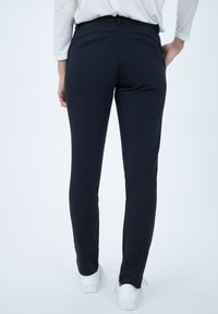 Pantaloni fitted blu realizzati in tessuto elasticizzato, con due tasche posteriori e una superficie liscia, abbinati a sneakers bianche.