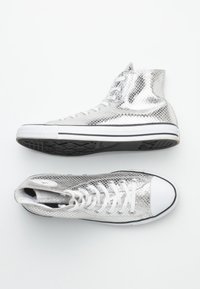 Vysoké tenisky s metalickým stříbrným hadím vzorem, bílými tkaničkami, bílými špičkami a černými gumovými podrážkami na bílém pozadí.