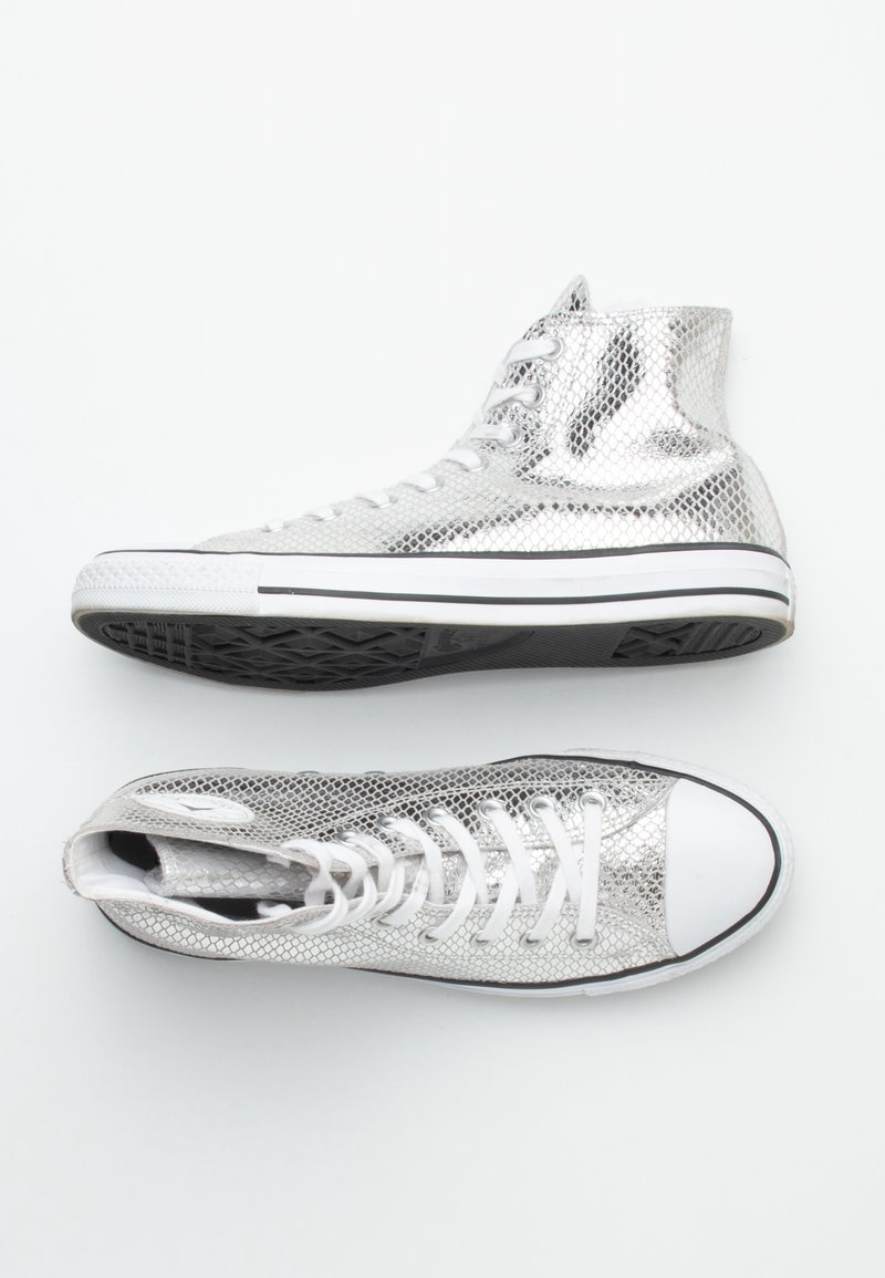 Vysoké tenisky s metalickým stříbrným hadím vzorem, bílými tkaničkami, bílými špičkami a černými gumovými podrážkami na bílém pozadí.