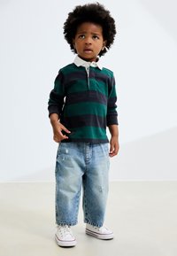 Rohelise ja tumesinise triibulise pika varrukaga polosärk valge kraega, kombineeritud helesiniste kulunud lahtiste teksade ja valgete tossudega.