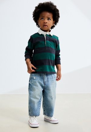 Zeleno-modře pruhovaná dlouhý rukáv polo košile s bílým límečkem, kombinovaná se světlomodrými roztrhanými volnými džínami a bílými teniskami.